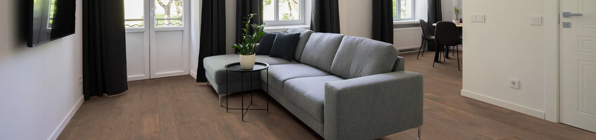 Modern living room with large windows, grey sectional sofa, and dark wood flooring
