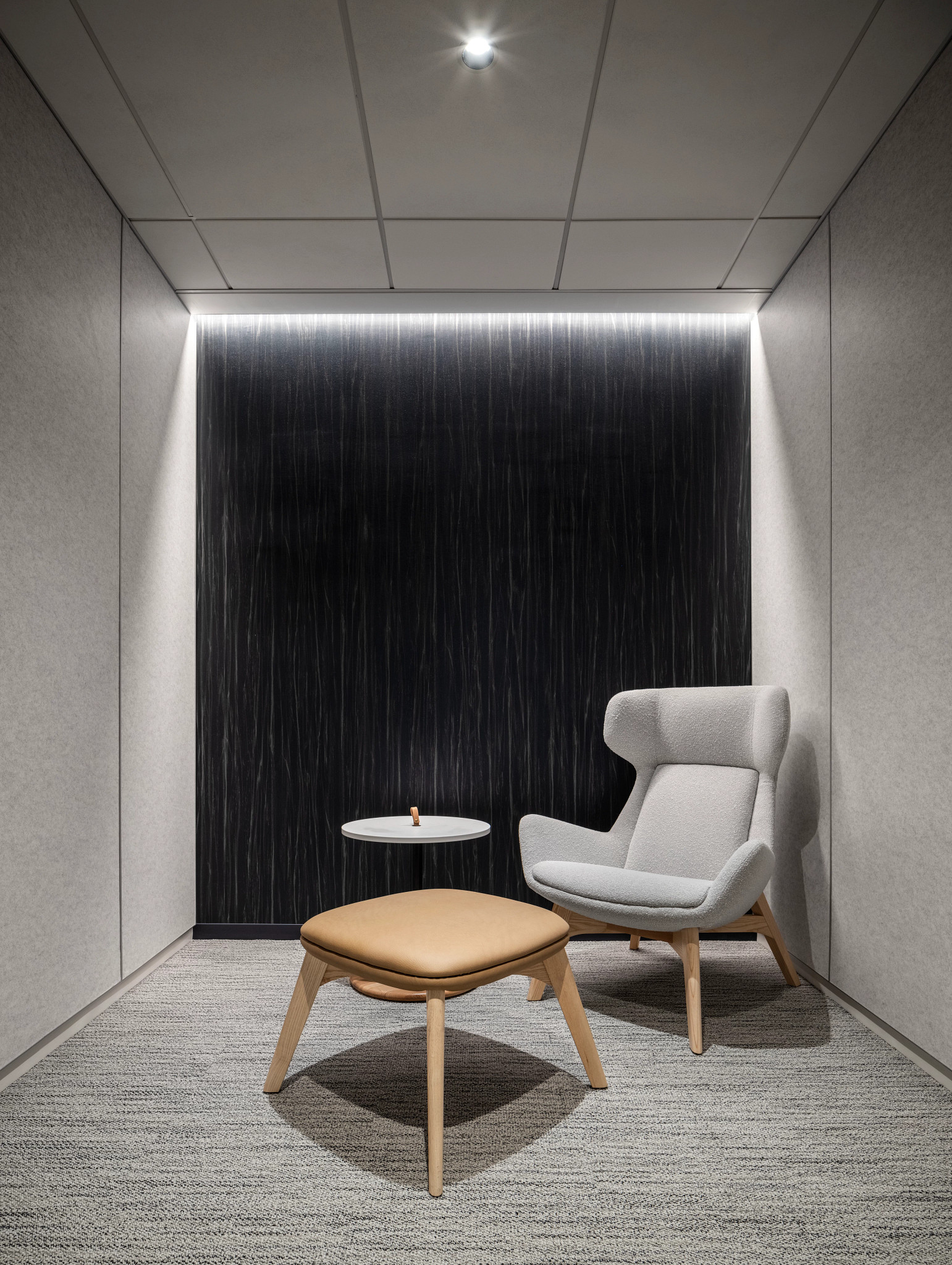 Modern office space with gray commercial carpet tile flooring, featuring a light gray armchair and a tan ottoman