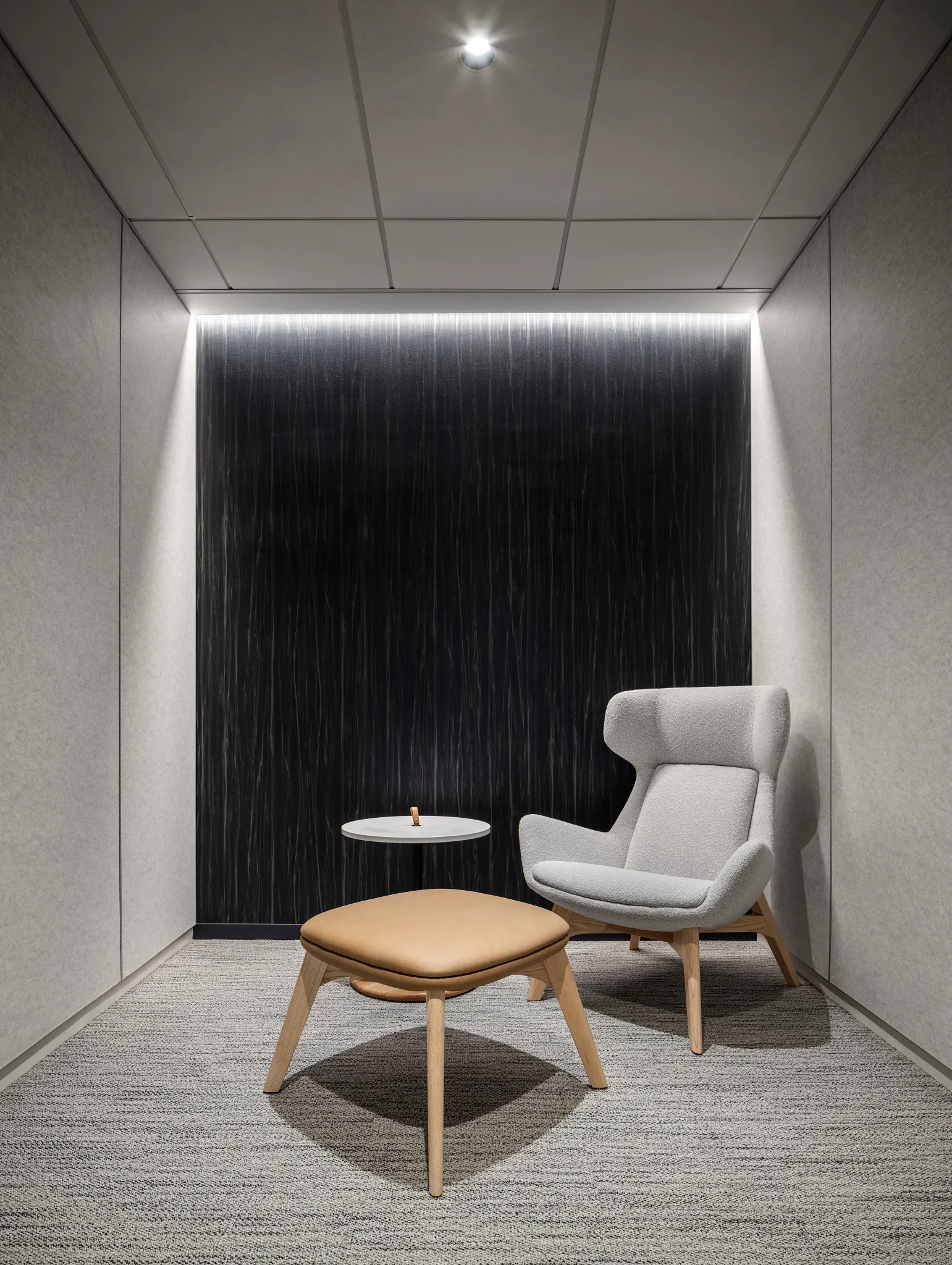 Modern office space with gray commercial carpet tile flooring, featuring a light gray armchair and a tan ottoman