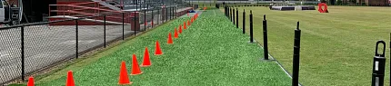 Artificial Turf Sports Field with Orange Cones and Bleachers Artificial turf lining a sports field with orange cones and bleachers in the background