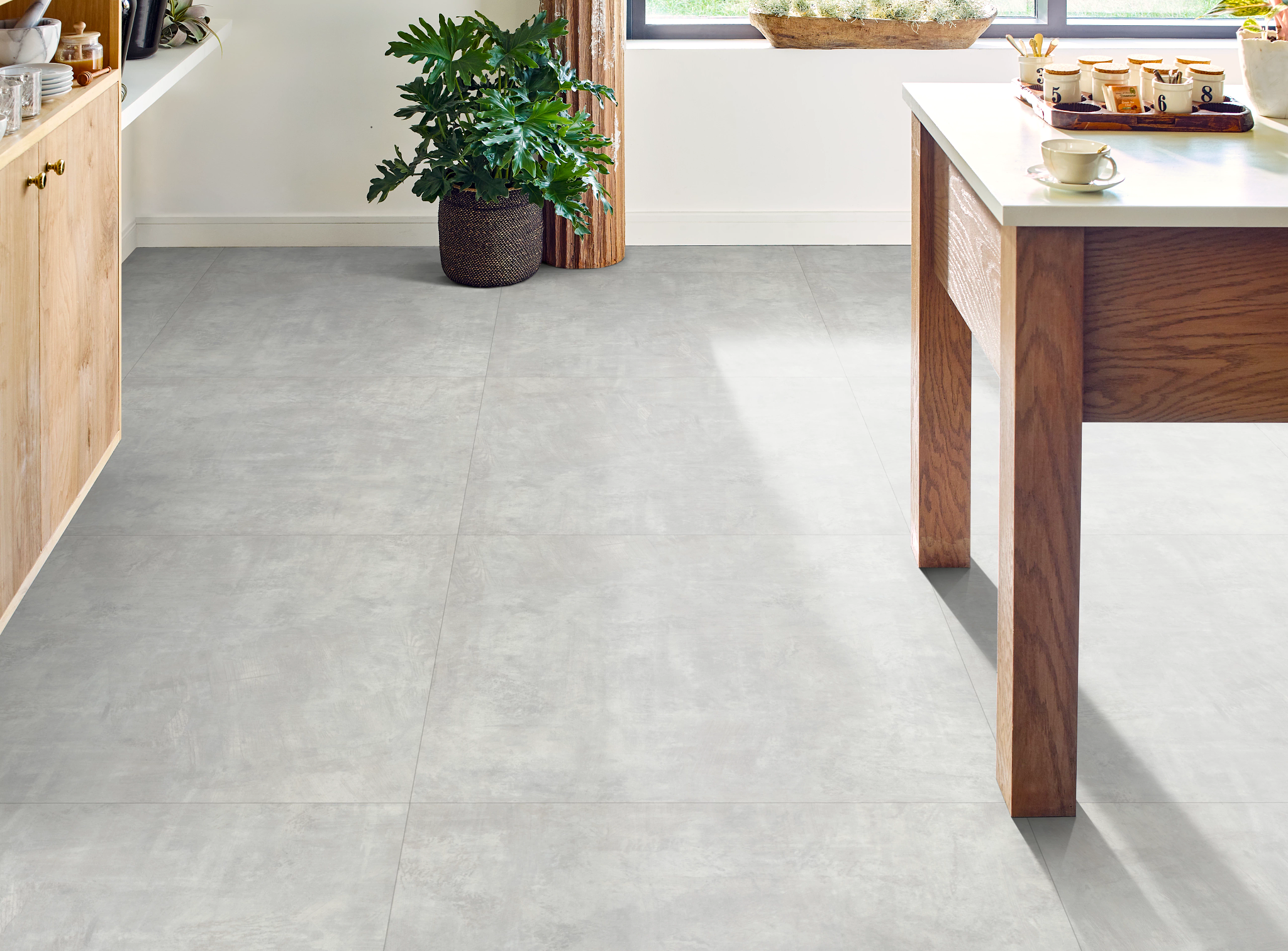 
  "Modern kitchen with high performance luxury vinyl tile flooring in light gray, featuring a wooden table and green plant"
)
