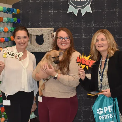 Pet-friendly carpet backdrop with women holding signs Group of women holding pet-themed signs in front of a patterned carpet backdrop