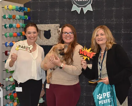 Pet-friendly carpet backdrop with women holding signs Group of women holding pet-themed signs in front of a patterned carpet backdrop