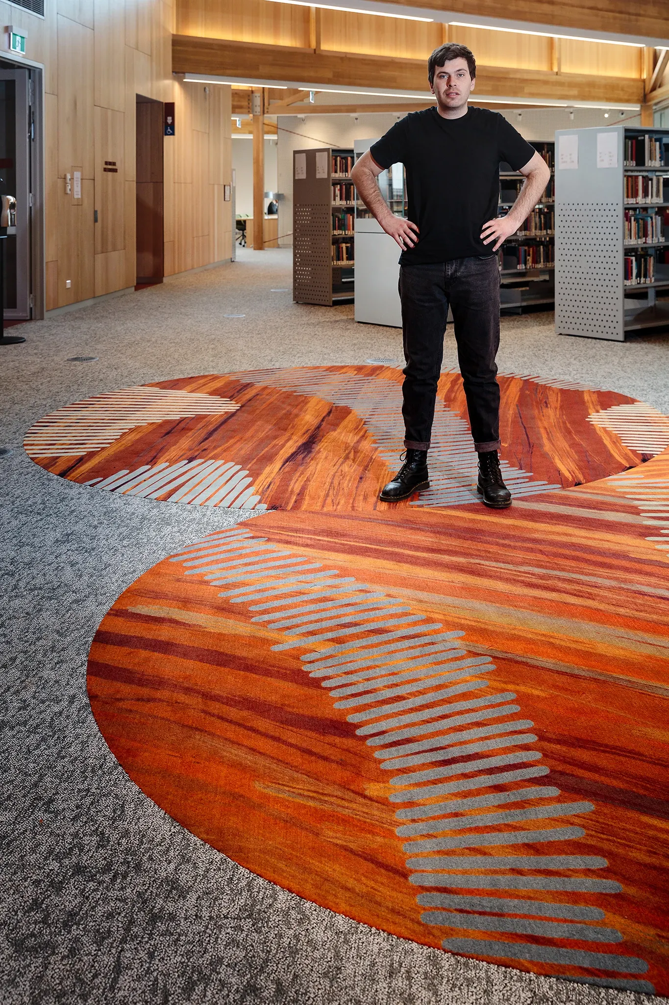 Artist standing within the University of Tasmania library on a custom flooring installation inspired by Indigenous storytelling and place-based design.