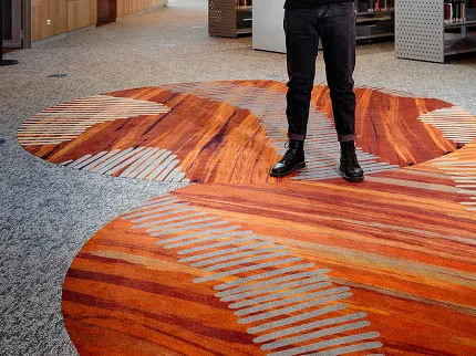 University of Tasmania Design Collaboration and Custom Flooring Installation | Shaw Contract Artist standing within the University of Tasmania library on a custom flooring installation inspired by Indigenous storytelling and place-based design.