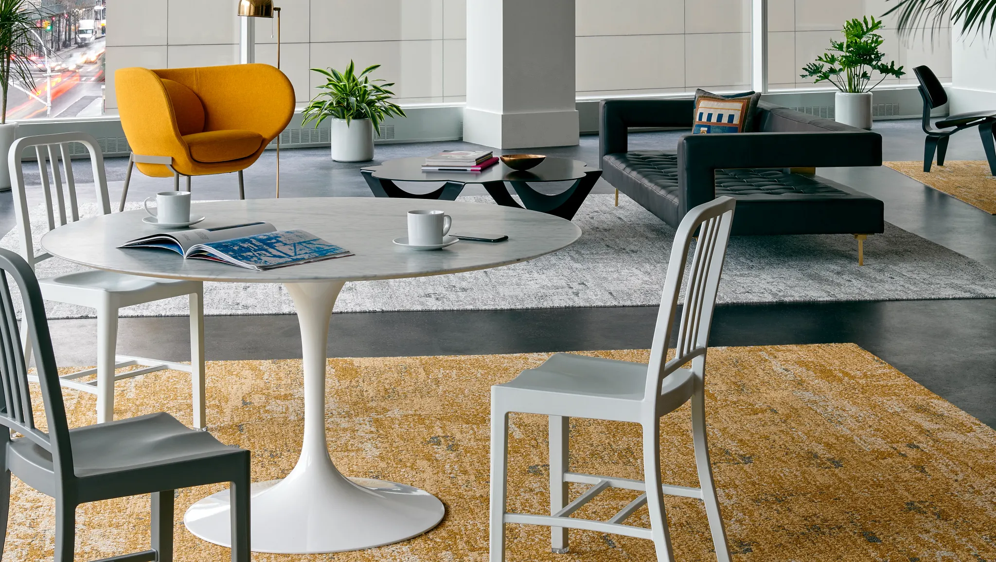 Modern office space with large windows, featuring a gray textured carpet, a yellow armchair, a black sofa, and indoor plants