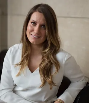 Woman in a white blouse sitting against a beige wall