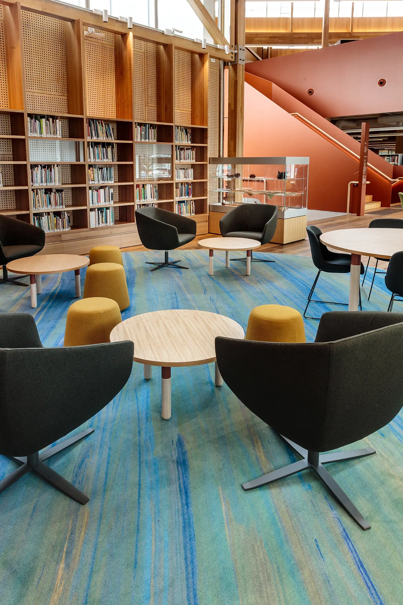 Collaborative learning space within the University of Tasmania library featuring custom blue patterned flooring, circular tables, lounge seating and integrated book collections.
