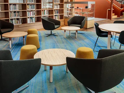 University of Tasmania Library Learning Space with Custom Flooring Design | Shaw Contract Collaborative learning space within the University of Tasmania library featuring custom blue patterned flooring, circular tables, lounge seating and integrated book collections.