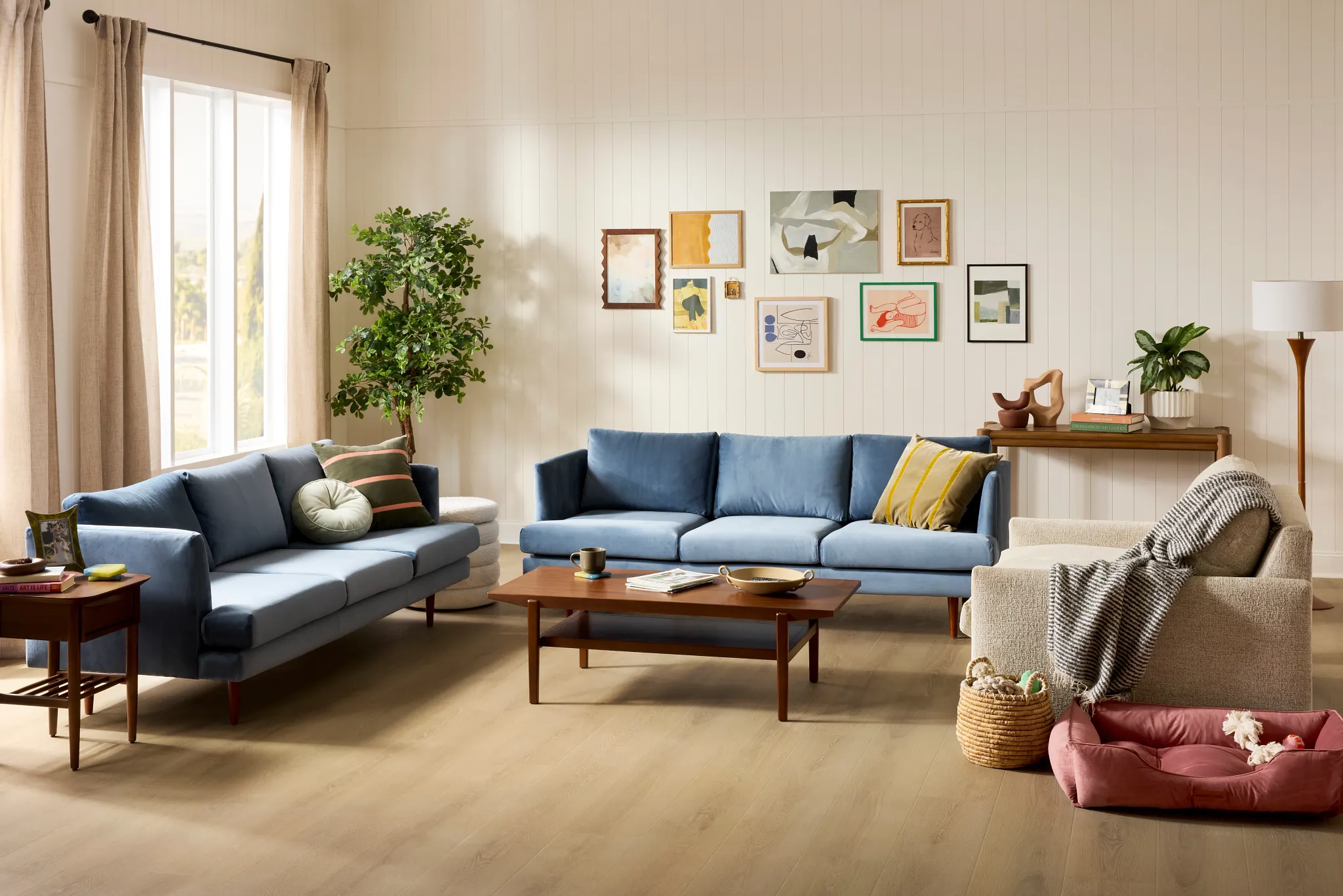 Modern living room with brown wood-look flooring, featuring a beige armchair, a light wood coffee table, and a gray sofa with decorative pillows
