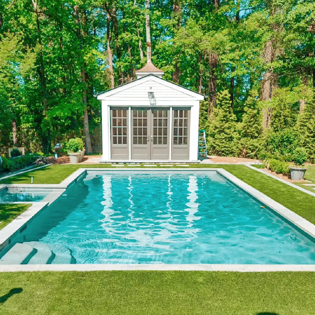 Outdoor swimming pool with surrounding greenery and pool house