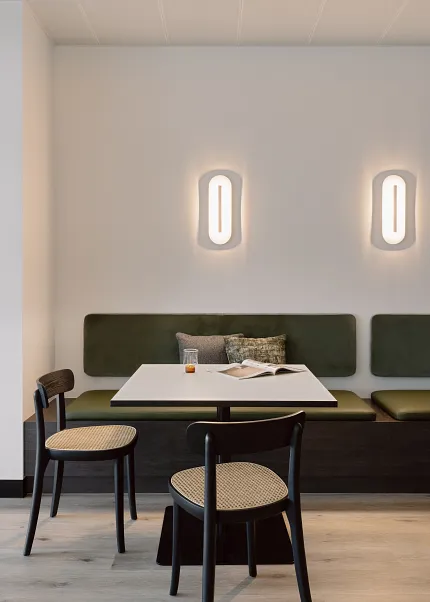 Hospitality seating area with contemporary design and light wood flooring Modern seating area with green cushioned bench, black chairs, and light wood flooring in a hospitality setting