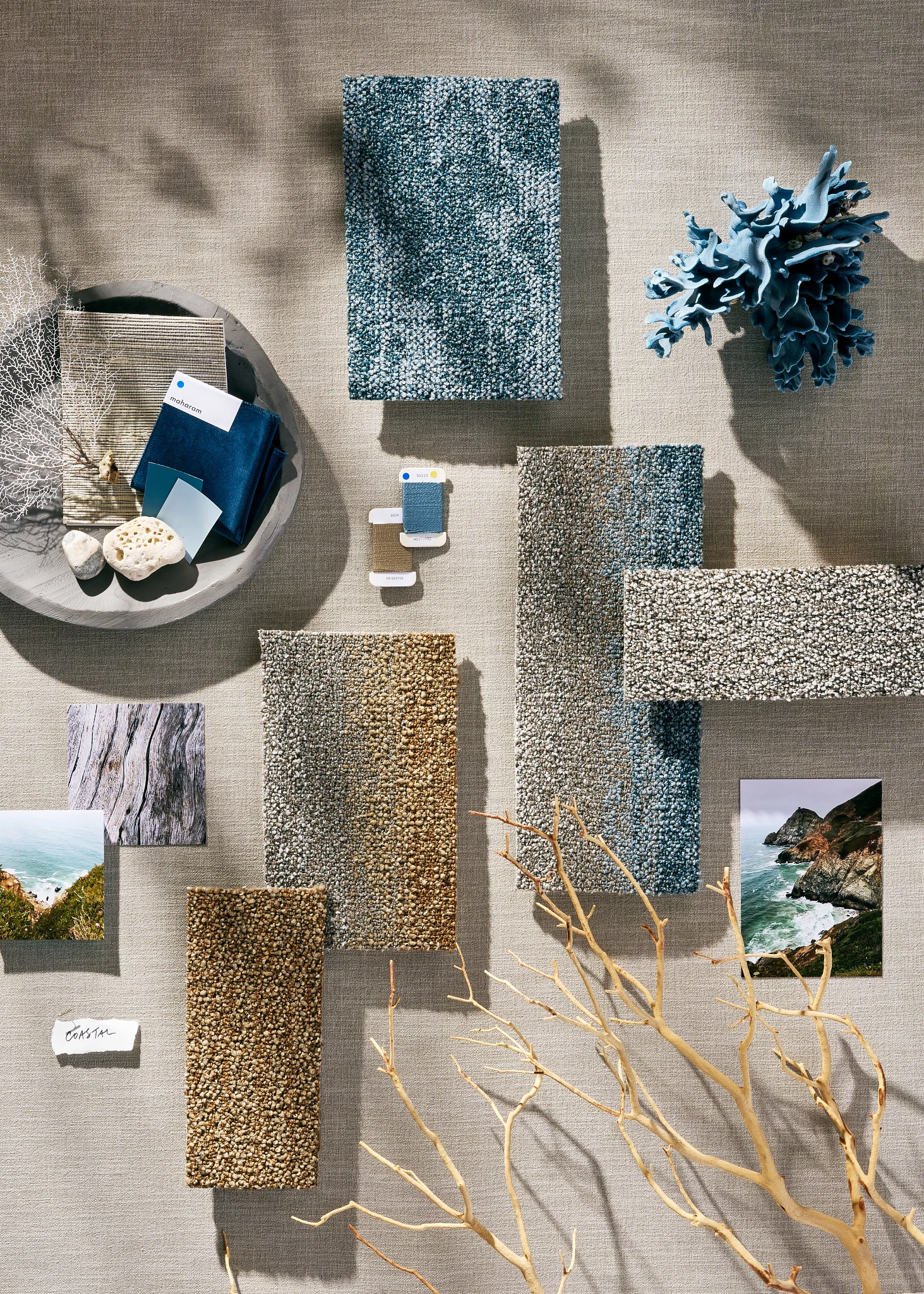 Assorted carpet swatches in shades of blue, purple, and black with natural elements and fabric samples on a textured surface