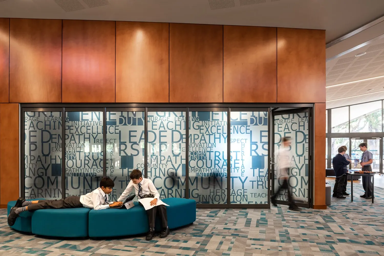 Education facility with modern design featuring commercial carpet tile flooring in a geometric pattern, teal seating, and wooden wall panels