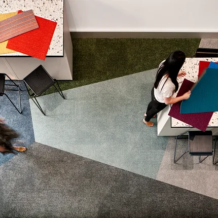 Modern Education Facility with Geometric Patterned Commercial Carpet Tile and Terrazzo Table Overhead view of a modern education facility with geometric patterned commercial carpet tile in shades of blue, green, and gray, featuring two women interacting with colorful fabric swatches on a terrazzo table