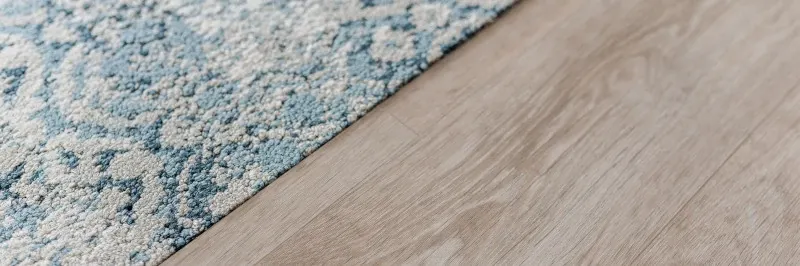 Close-up of a light wood flooring next to a blue and white textured carpet