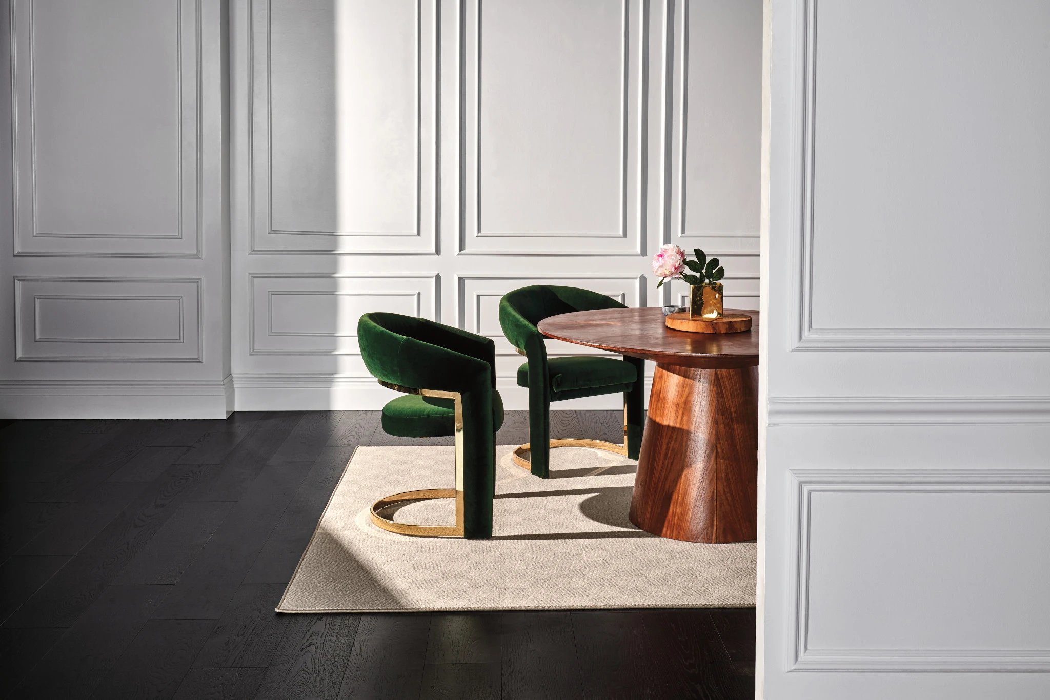 Elegant dining room with dark hardwood flooring and a beige area rug under a wooden table with green velvet chairs