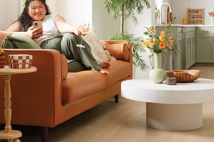 Homely Living Room with Durable Light Wood Flooring for Everyday Comfort Cozy living room with light wood flooring, featuring a comfortable brown sofa, a white round coffee table, and a lush green plant