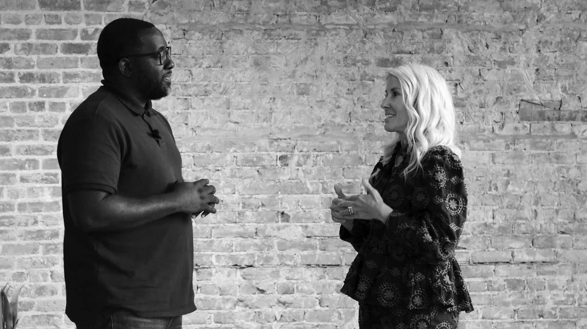 Two people conversing in front of a textured brick wall