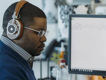 Modern office environment with focused employee using technology Office workspace with a person wearing headphones working on a computer