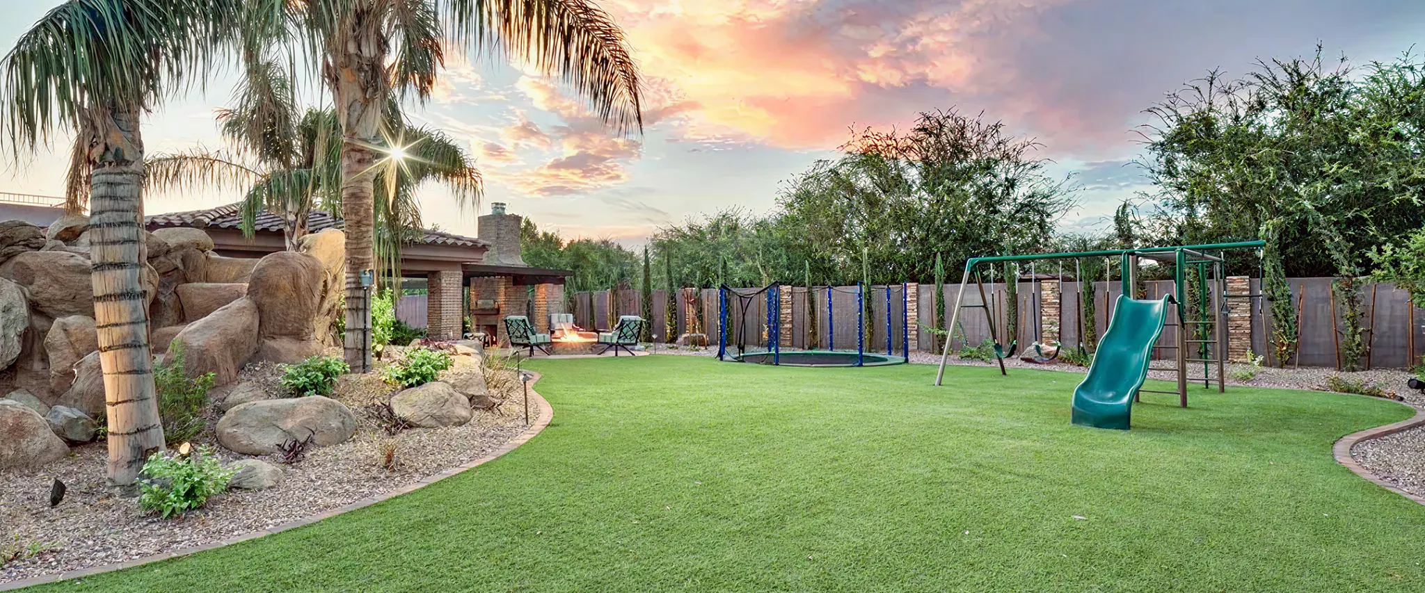 Backyard with artificial grass, palm trees, and playground at sunset