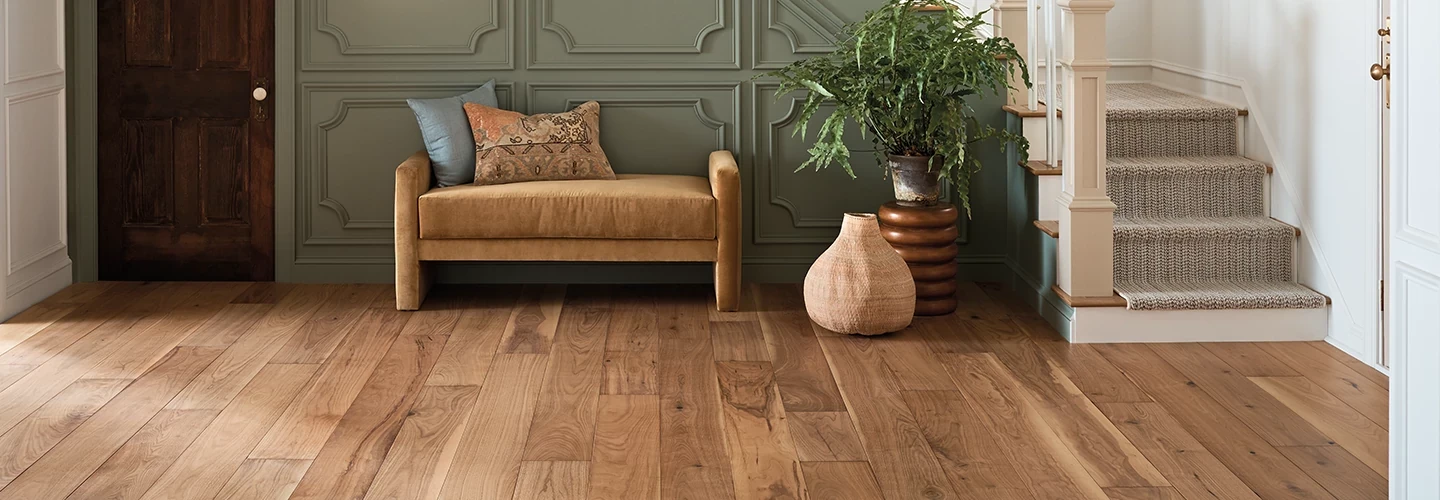 living room with hardwood floor with a tan couch decorative pillows and a potted plant beside a staircase with carpeted steps