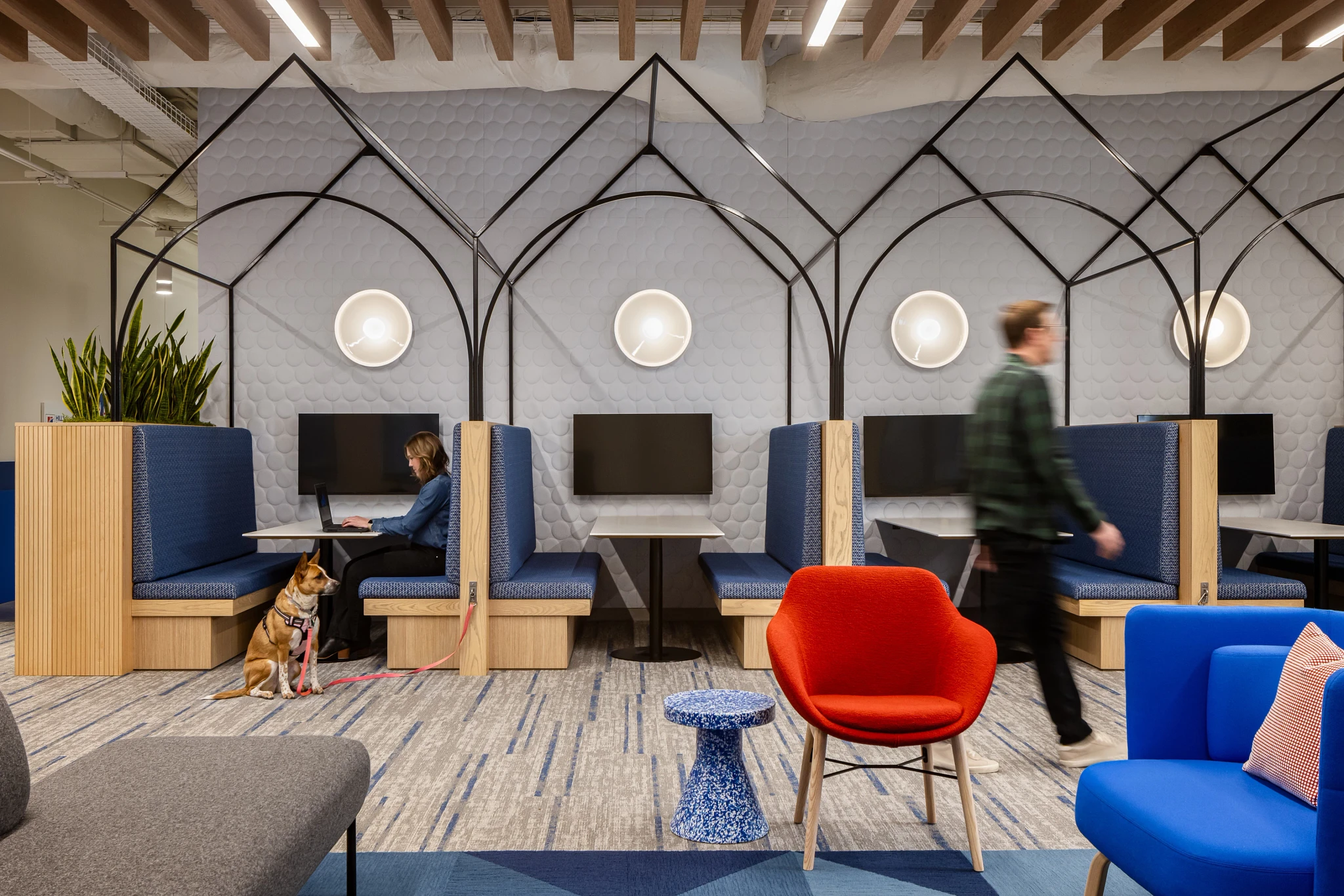 Modern workplace lounge area with blue and gray commercial carpet tile, featuring private seating booths, a red chair, and a blue side table