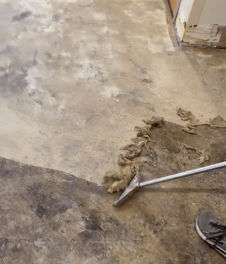 Floor preparation process with adhesive removal tool and worn sneakers visible