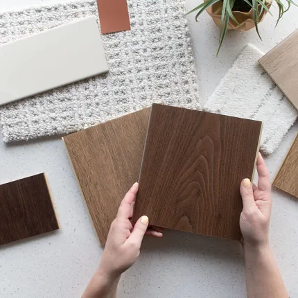Wood Look Vinyl Flooring Swatch with Assorted Samples Hands holding a wood look vinyl flooring swatch surrounded by various flooring samples in shades of brown, beige, and cream