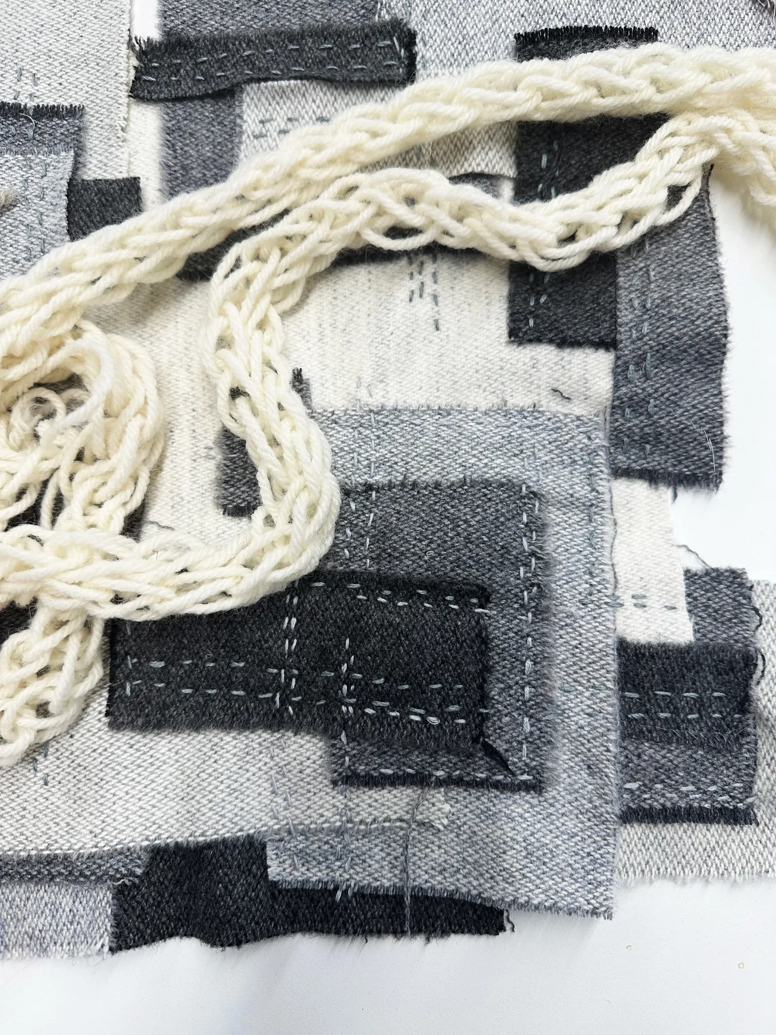 Textured fabric swatch with black, grey, and white patches and braided white yarn