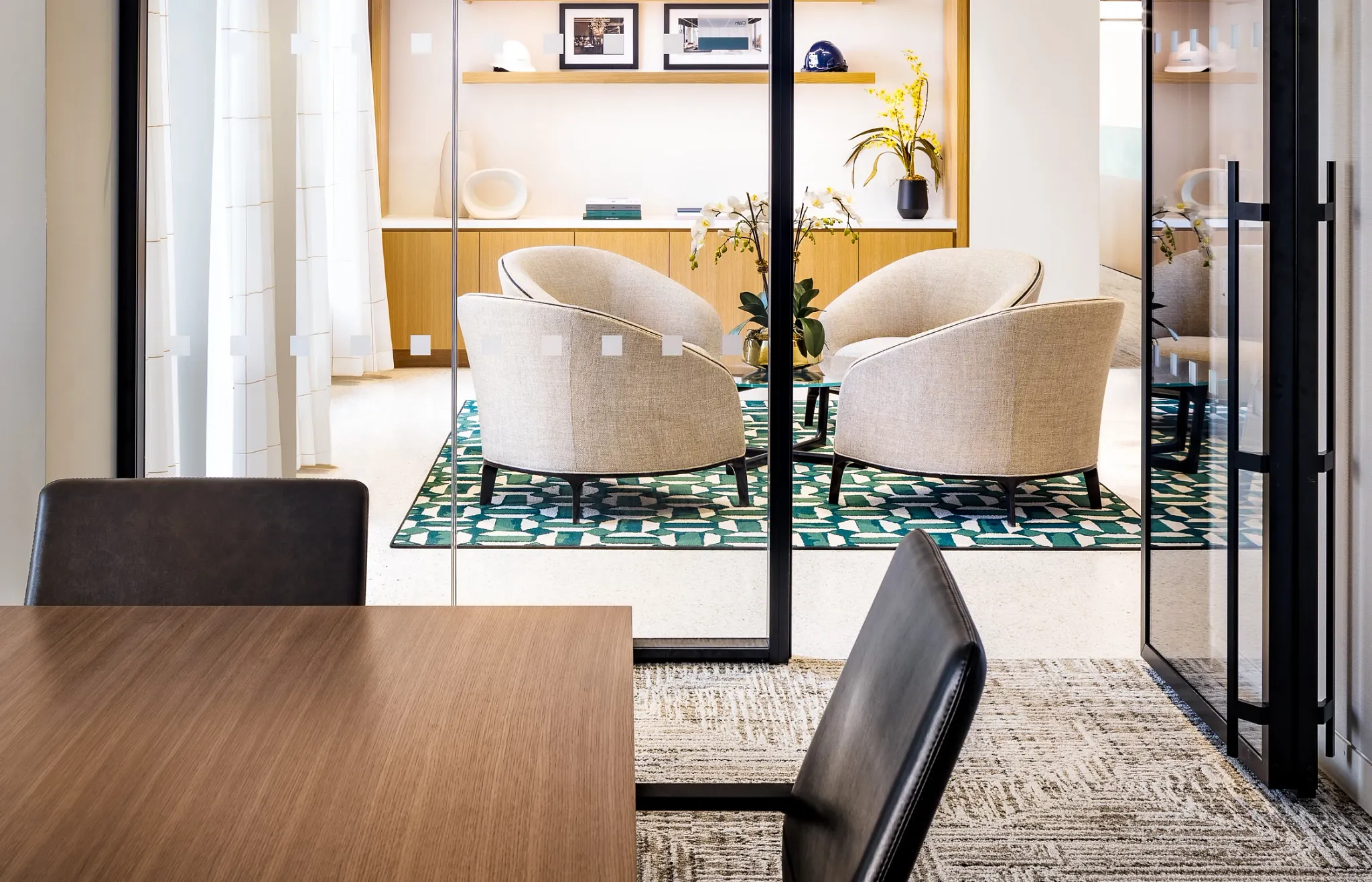 Modern workplace interior with glass partitions, beige armchairs, and a patterned green rug