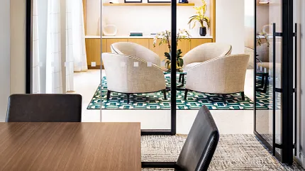 Contemporary Workplace Design with Glass Partitions and Stylish Furnishings Modern workplace interior with glass partitions, beige armchairs, and a patterned green rug