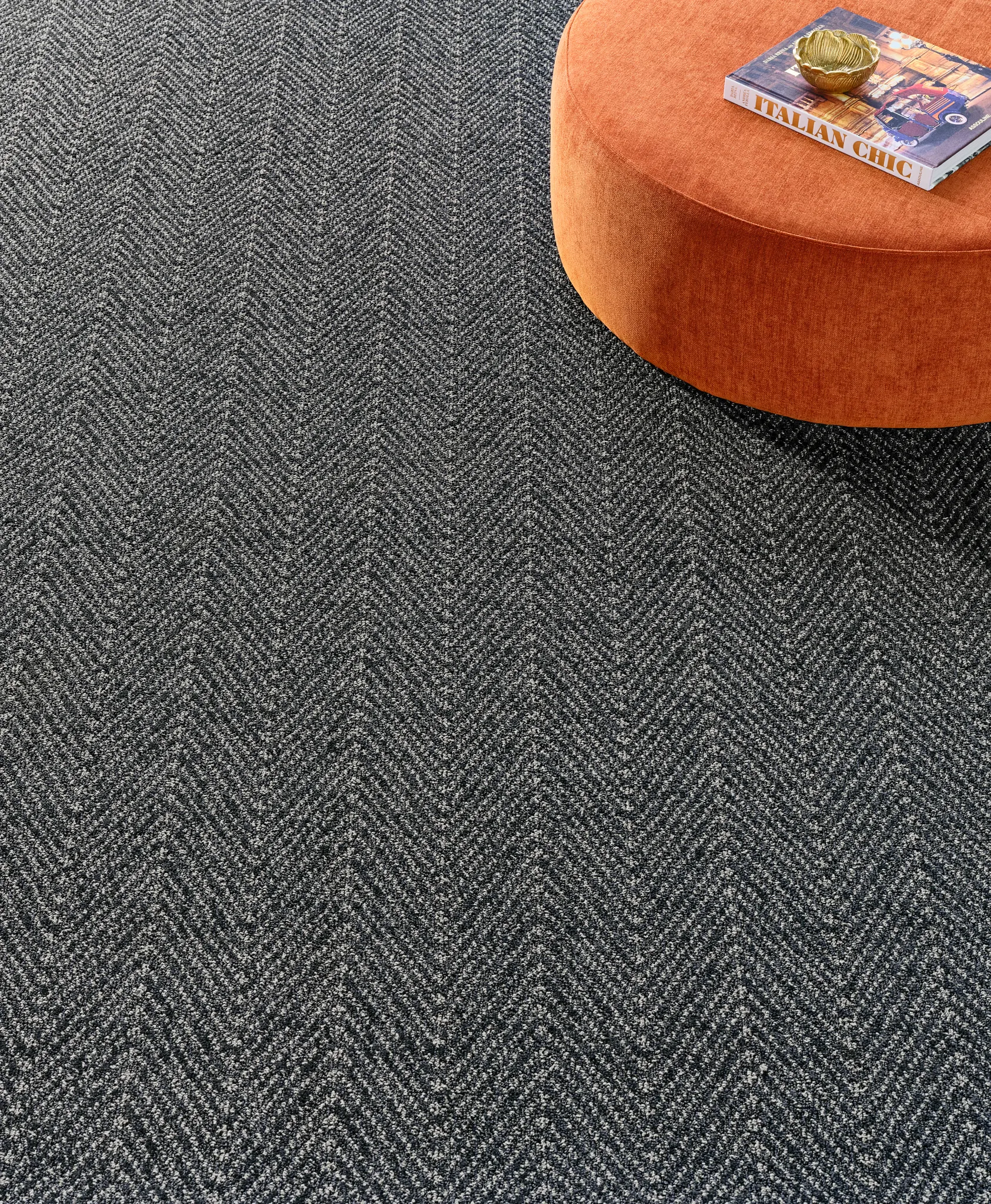 Broadloom carpet in herringbone pattern with orange ottoman