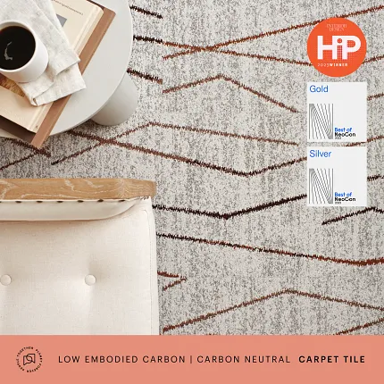Low Embodied Carbon Carpet Tile with Geometric Design - Award-Winning Commercial Flooring Modern commercial carpet tile with geometric pattern in shades of gray and brown, featuring a coffee table with books and a cup of coffee