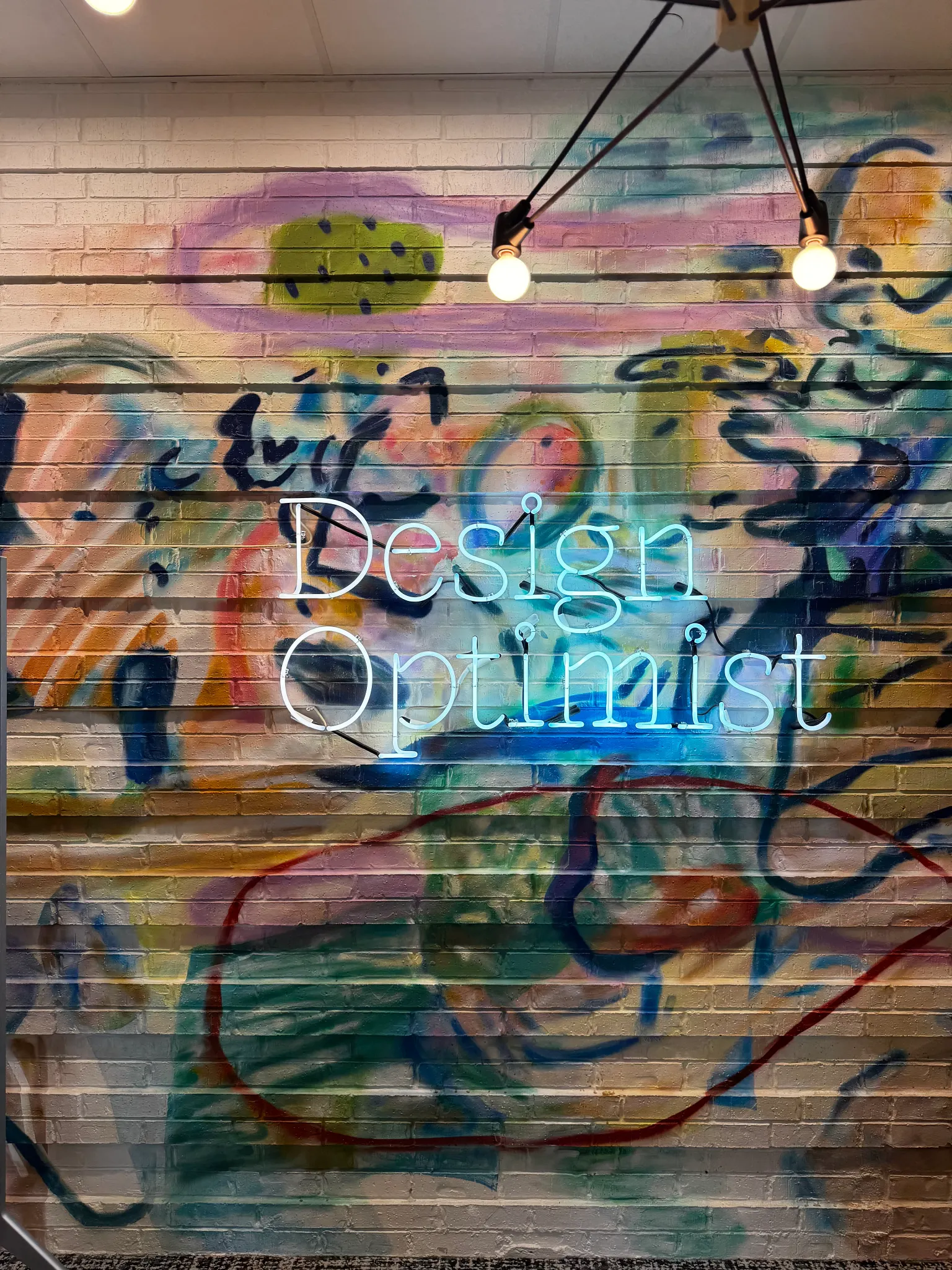 Colorful graffiti wall with neon sign reading "Design Optimist