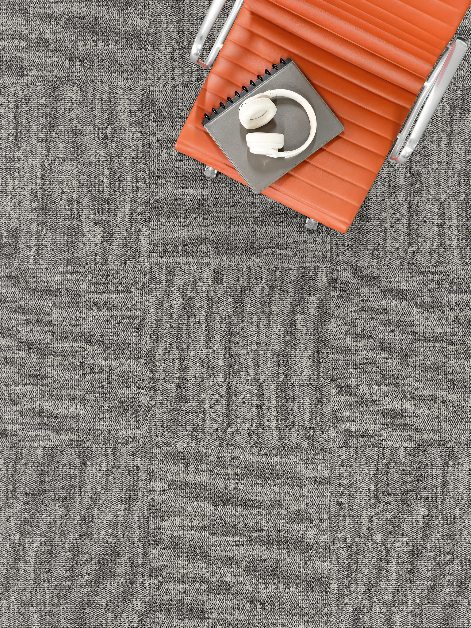 Overhead view of a modern office chair with an orange leather seat on a gray commercial carpet tile