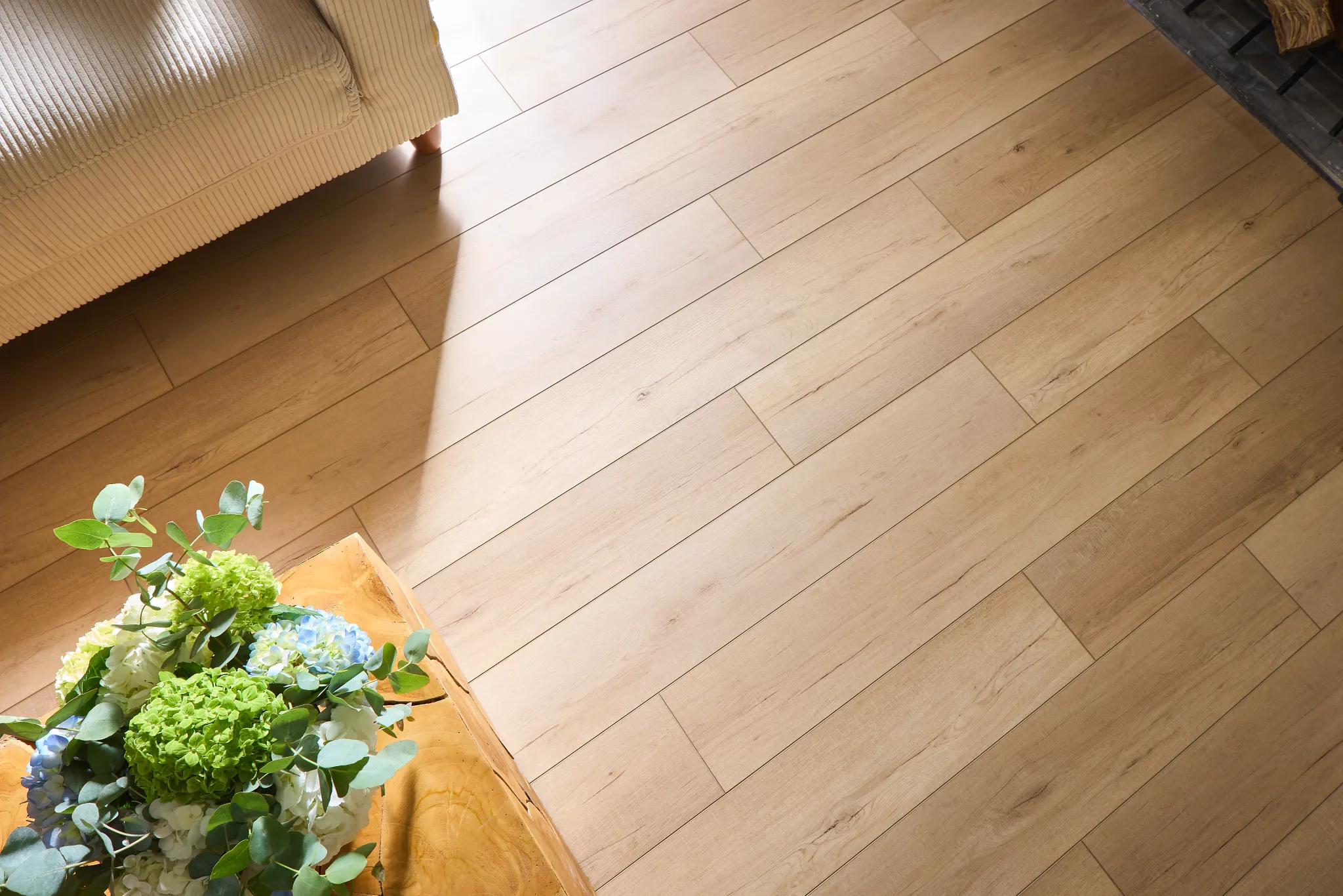 Light wood look vinyl flooring in a cozy living room with a beige sofa and a wooden table with a floral arrangement