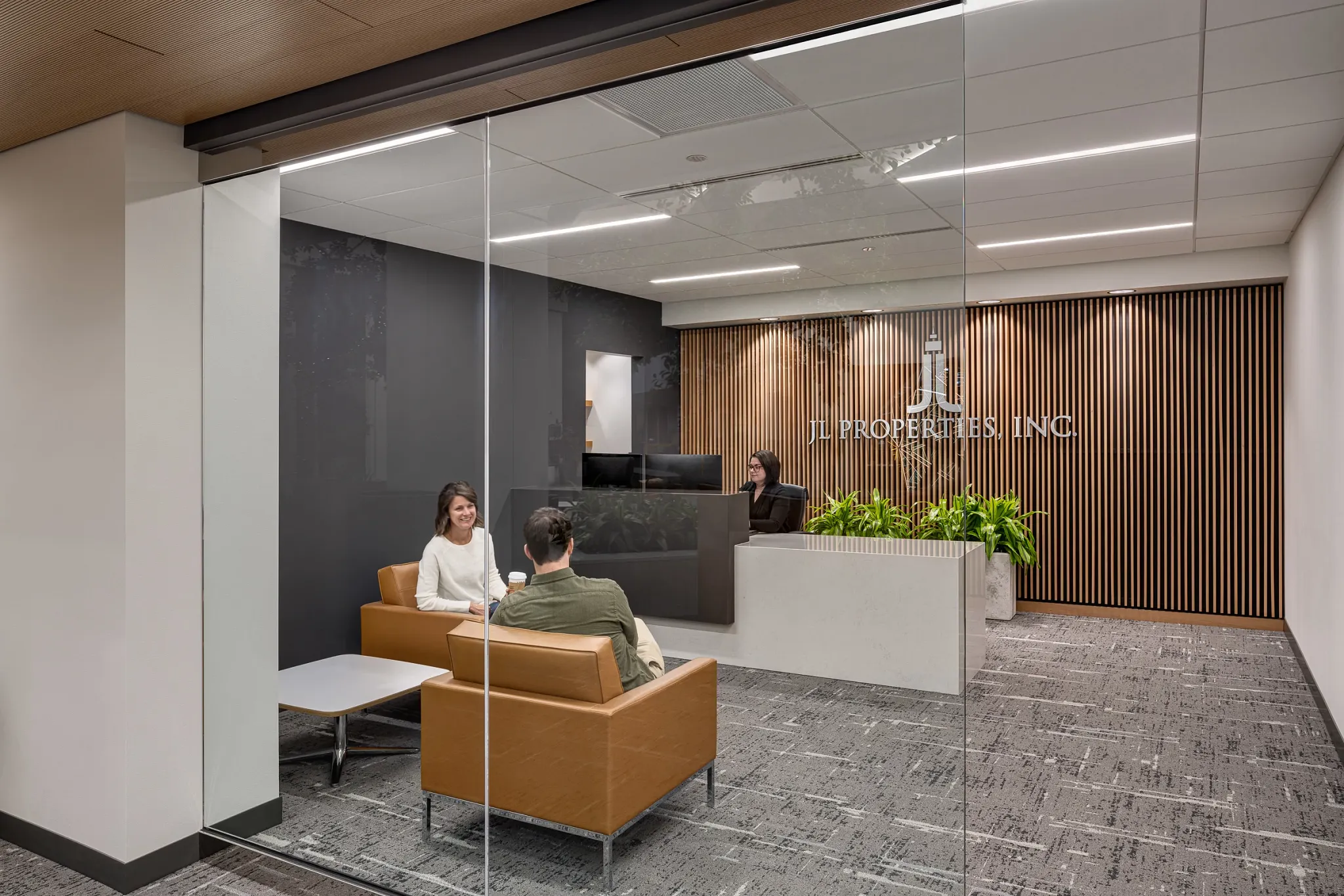 Modern office reception area with commercial carpet tile flooring, featuring a glass wall, wooden slat accent wall, and contemporary seating.