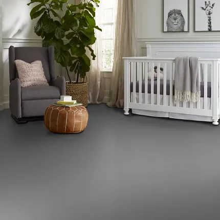 Gray flooring in a stylish nursery room with white crib and gray armchair Modern nursery room with gray flooring, white crib, gray armchair, and brown ottoman