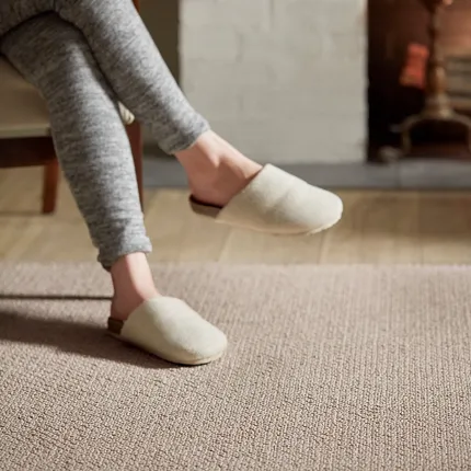 Comfortable and Durable Beige Carpet for Everyday Home Comfort Cozy living room scene with a person in gray leggings and cream slippers enjoying a warm drink on a textured beige carpet