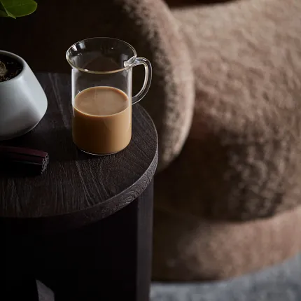 Cozy Living Room with Dark Wood Table and Gray Carpet Cozy living room scene with a dark wooden side table, a glass mug of coffee, and a plush beige chair on a soft gray carpet