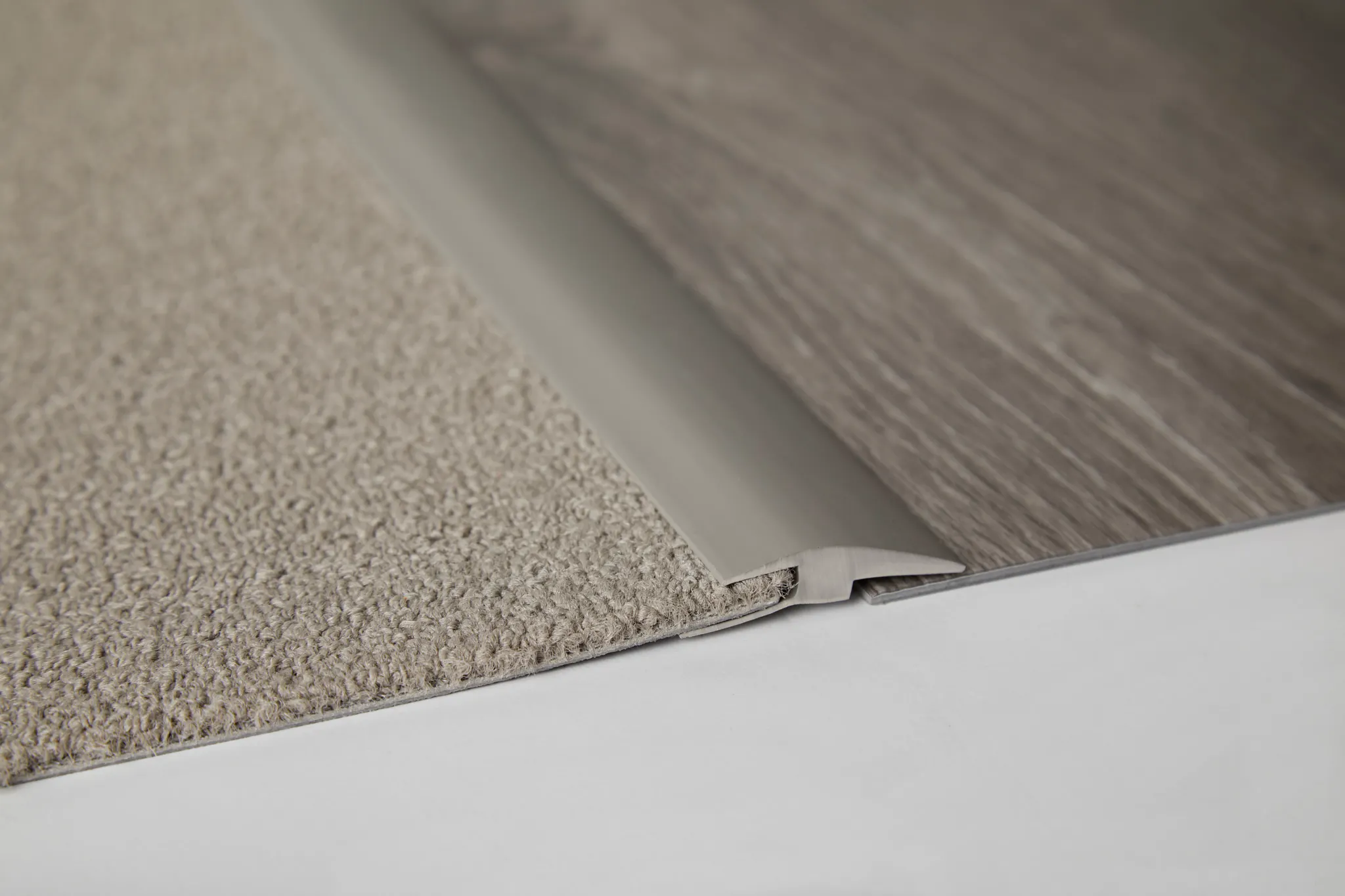 Close-up of a transition strip between beige carpet and gray wood-look flooring