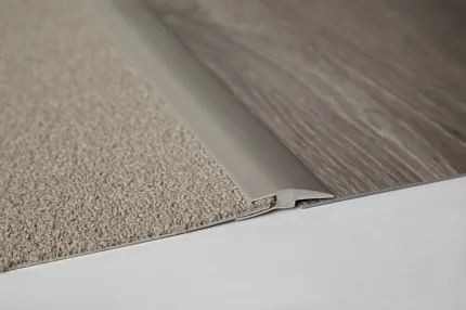 Transition Strip for Carpet and Wood-Look Flooring Close-up of a transition strip between beige carpet and gray wood-look flooring