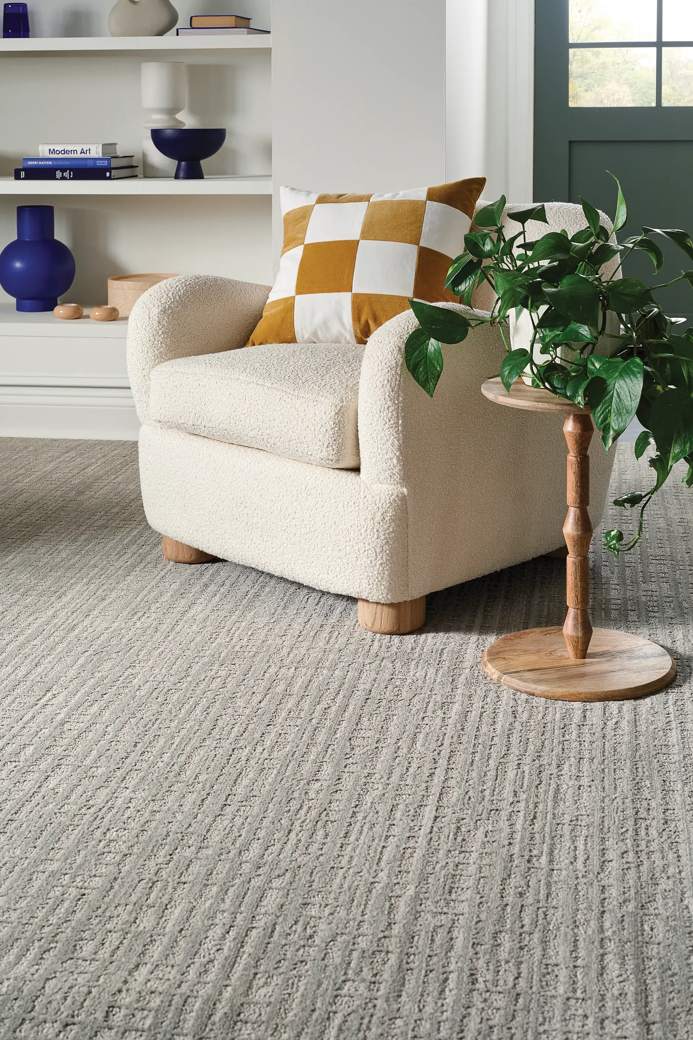 Cozy living room with textured carpet flooring, featuring a cream armchair, wooden side table, and a green plant