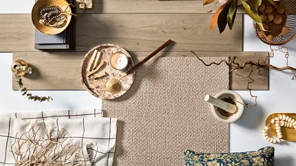 Light Brown Laminate Flooring and Beige Carpet Swatch in a Cozy Home Setting Overhead view of a cozy home setting featuring light brown laminate flooring and beige carpet swatch, surrounded by decorative items like a candle, books, and a patterned pillow