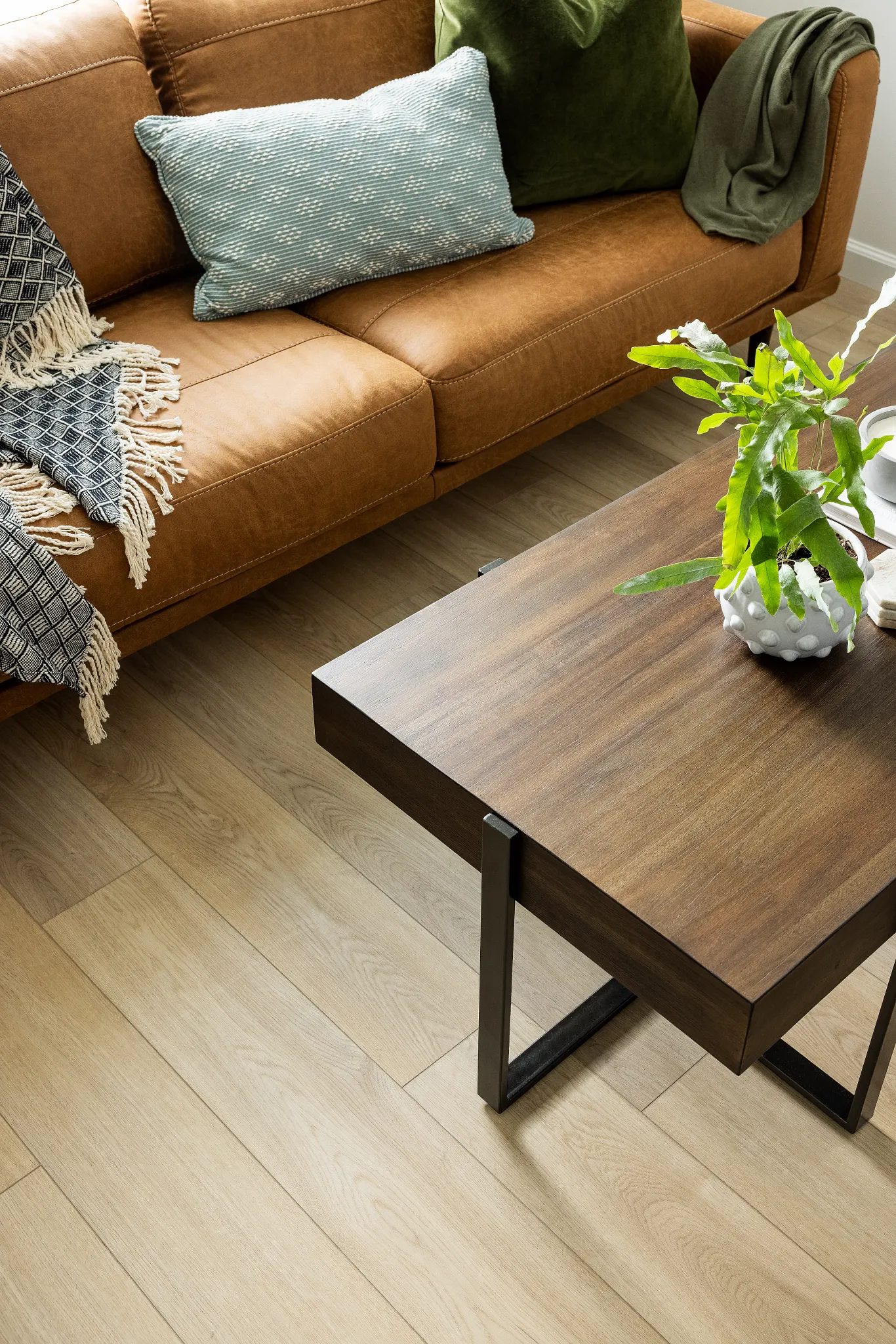 Modern living room with light oak wood flooring, brown leather sofa, and wooden coffee table with green plant