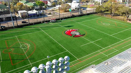 Artificial Turf Sports Field with Central Logo and Cityscape Background Aerial view of a sports field with artificial turf featuring a red and black logo in the center