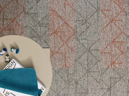 Geometric Pattern Commercial Carpet Tile in Gray and Orange with Teal Swatch. Commercial carpet tile with geometric pattern in gray and orange, featuring a teal fabric swatch and yarn samples on a beige table.
