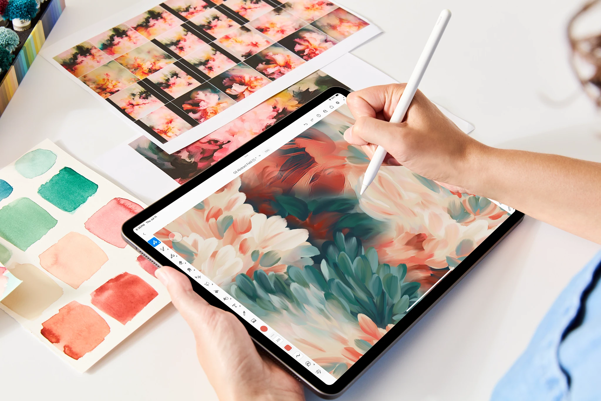 Person using a digital pen on a tablet to create floral artwork, surrounded by color swatches and printed floral designs
