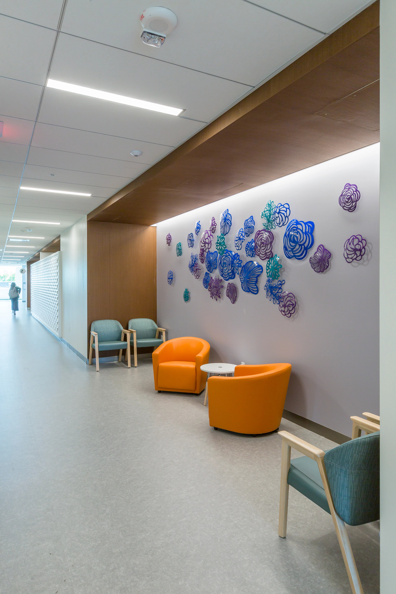 Healthcare facility hallway with PVC-Free Commercial Bio-Based Polyurethane Heterogeneous Tile flooring, featuring orange and blue chairs and colorful wall art